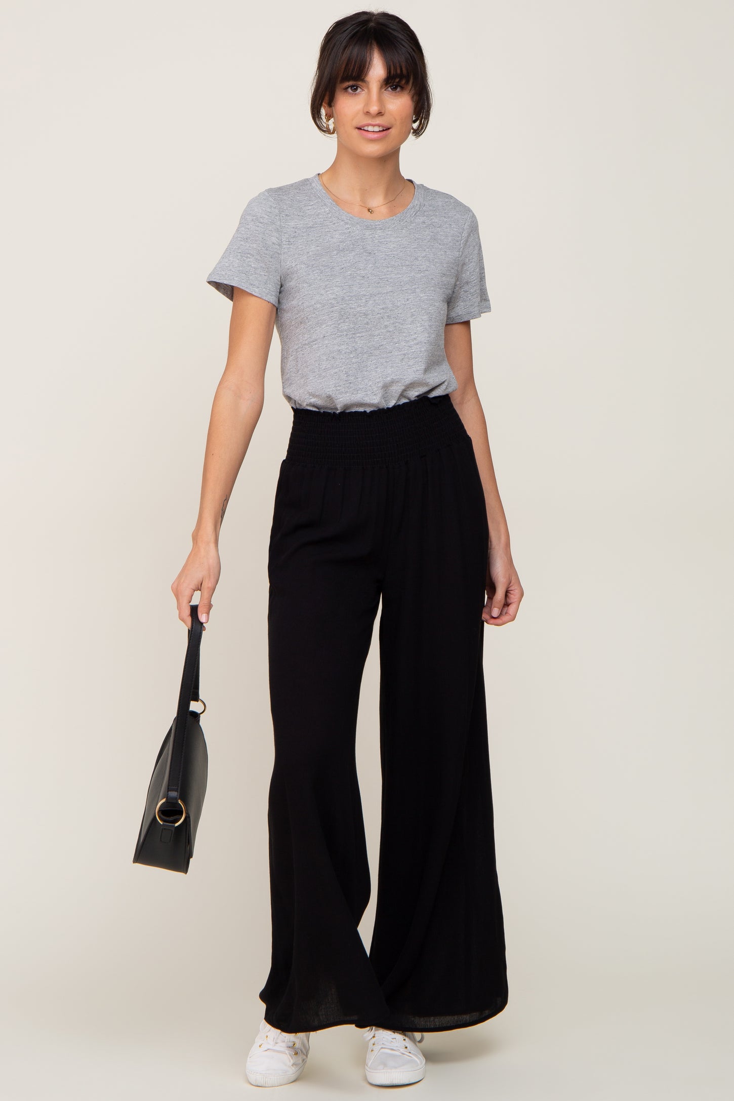 woman wearing a grey crew neck t-shirt and black wide-leg trousers holding a black handbag