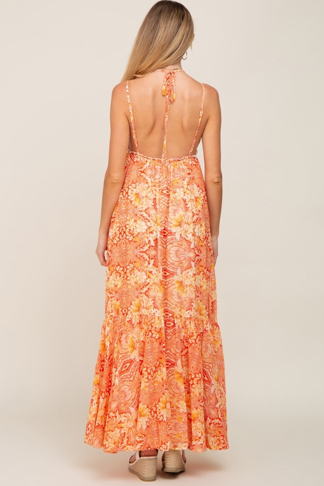 Woman from behind wearing an orange paisley print backless maxi dress with halter tie and wedge sandals