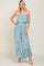 woman wearing a light blue strapless floral jumpsuit with wide legs and ruffle hem