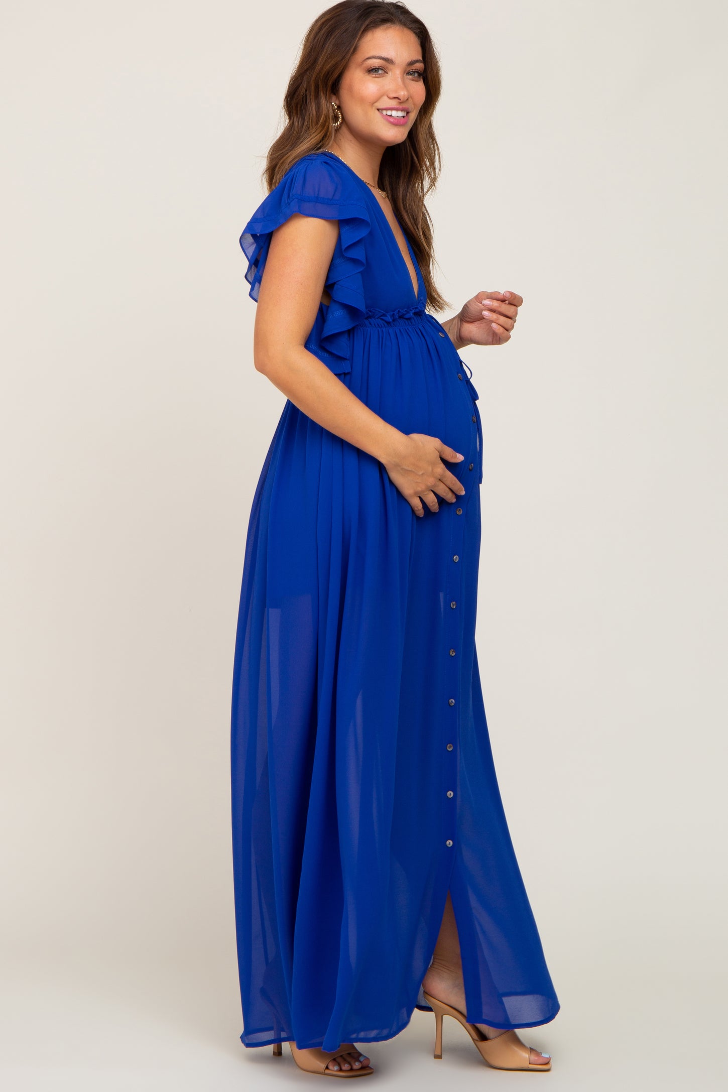woman wearing a royal blue maternity maxi dress with ruffle sleeves and a front slit, showing her baby bump