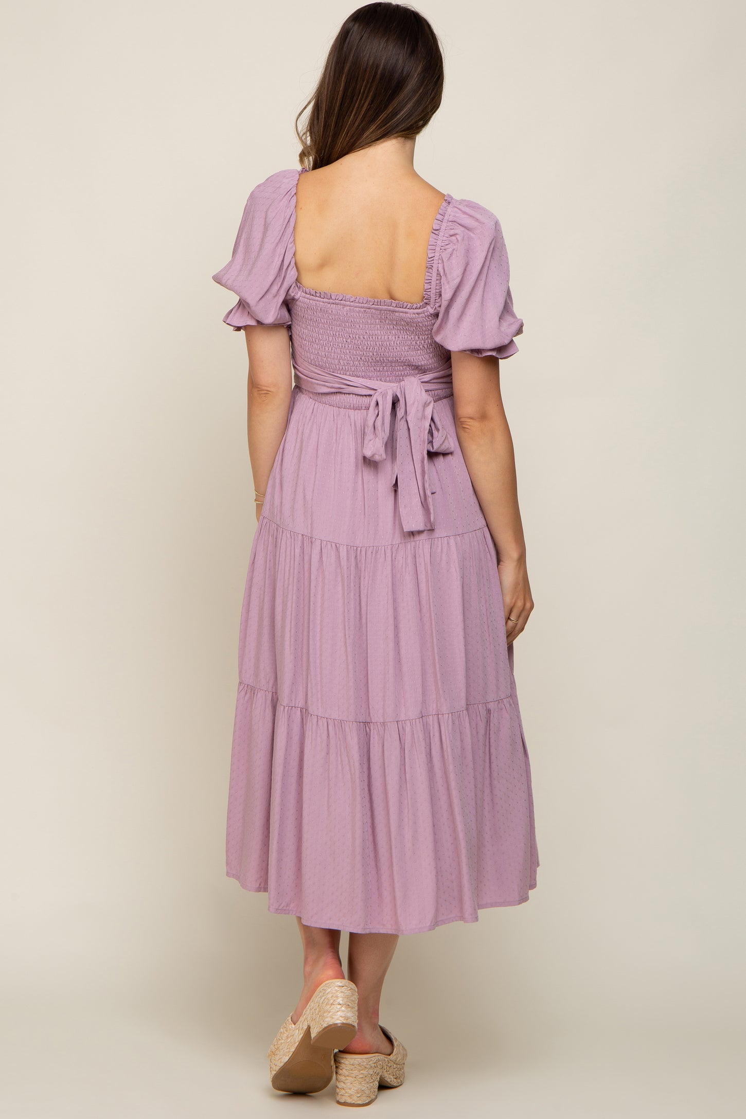 Back view of woman wearing a lavender tiered midi dress with smocked back and puff sleeves