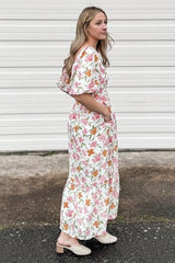 woman wearing a floral maxi dress with puff sleeves and pockets, standing on a pathway near a white backdrop