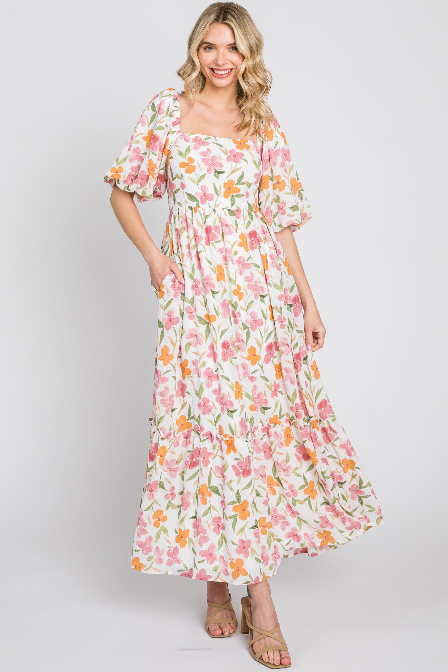 woman wearing a floral maxi dress with puff sleeves and pockets in pink, orange, and green colors