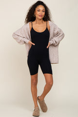 woman wearing a black ribbed bodysuit and oversized beige cardigan, paired with tan slippers