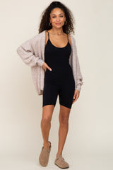 woman wearing a black sleeveless bodysuit and a light pink cardigan with a relaxed fit, styled with brown ankle boots