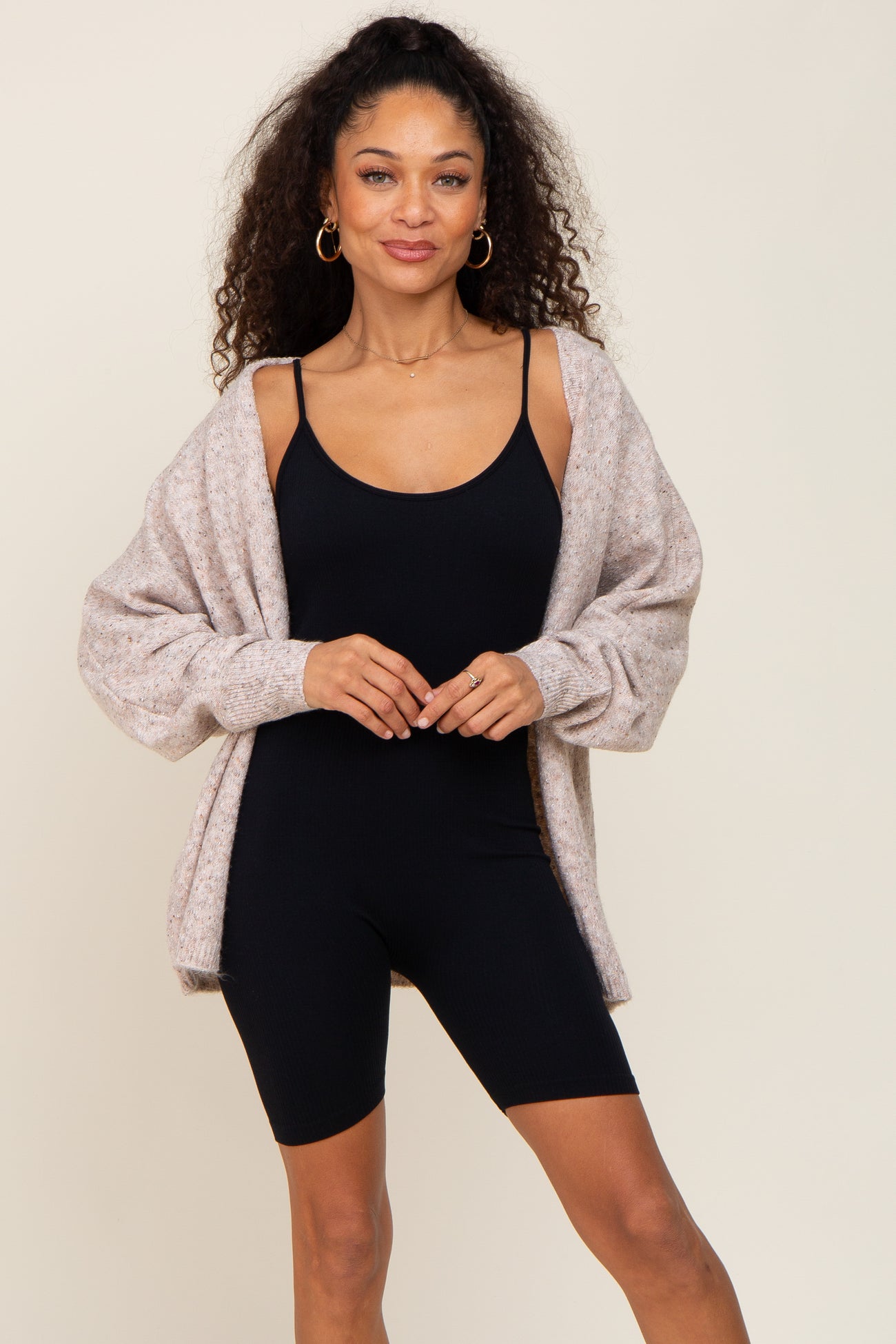 woman wearing a beige oversized cardigan over a black tank bodysuit and shorts