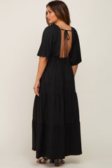 Woman wearing a black tiered maxi dress with an open back and tie detail