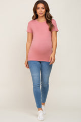 woman wearing a pink short sleeve maternity top and blue skinny jeans showing her baby bump