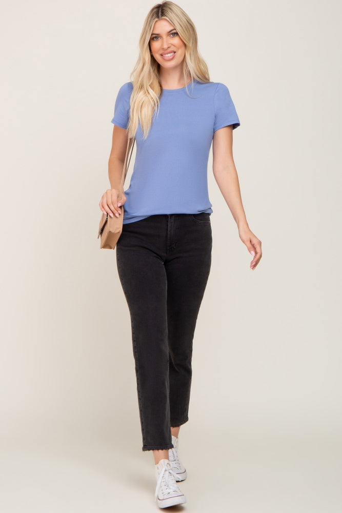 woman wearing a light blue short sleeve top and black jeans, holding a small bag and walking towards the camera