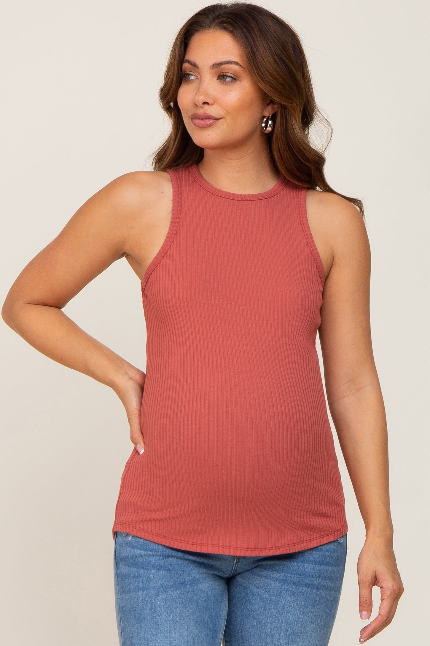 woman wearing a rust ribbed maternity tank top and showing her baby bump while posing with one hand on her hip