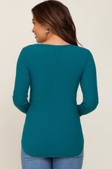 woman wearing a teal long sleeve maternity top, viewed from the back, with a curved hemline and ribbed texture