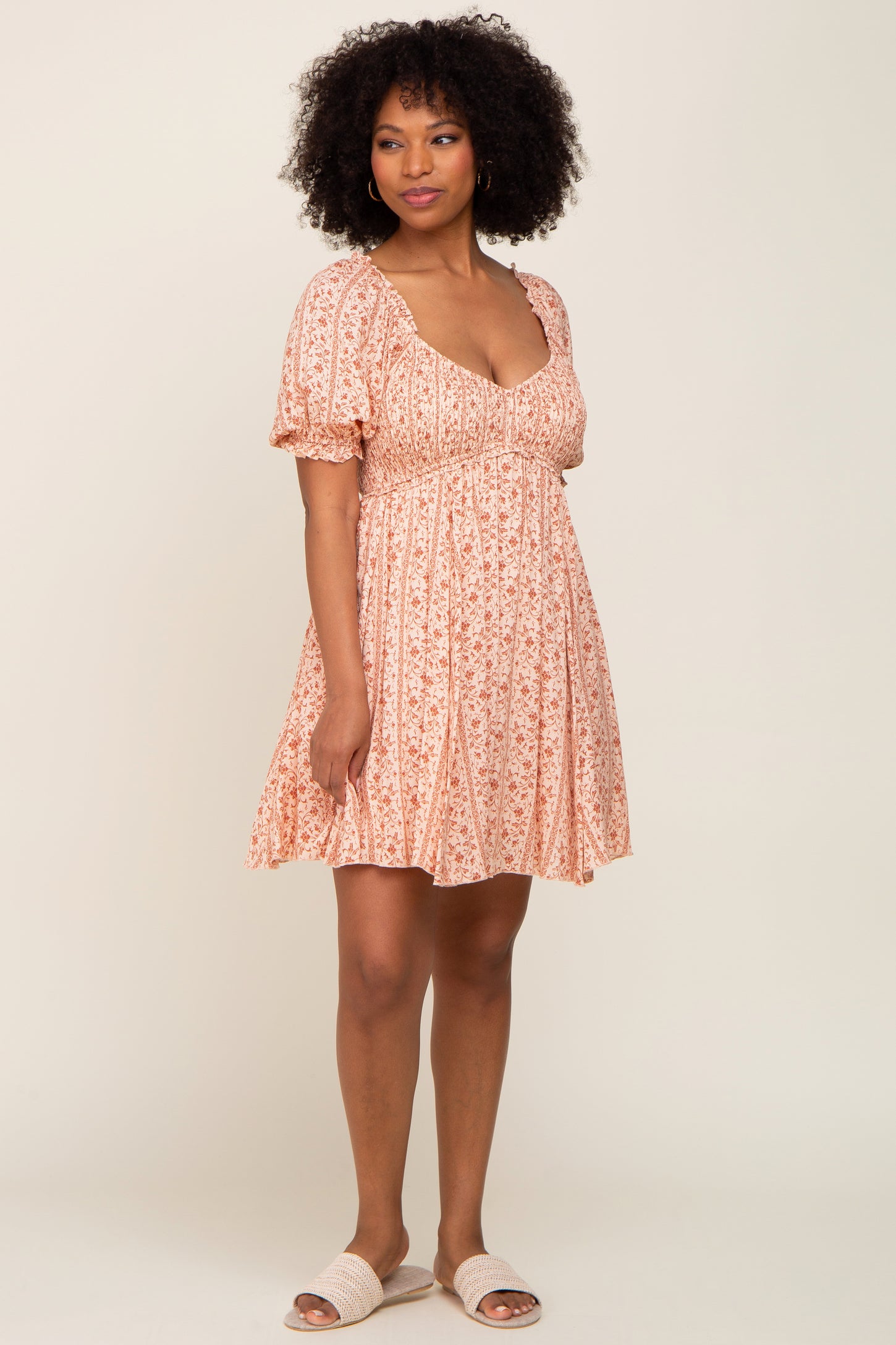 woman with afro hair wearing a pink floral puff sleeve mini dress and woven sandals