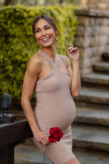woman wearing a beige ribbed maternity dress with a one-shoulder design and holding a red rose, showing her baby bump