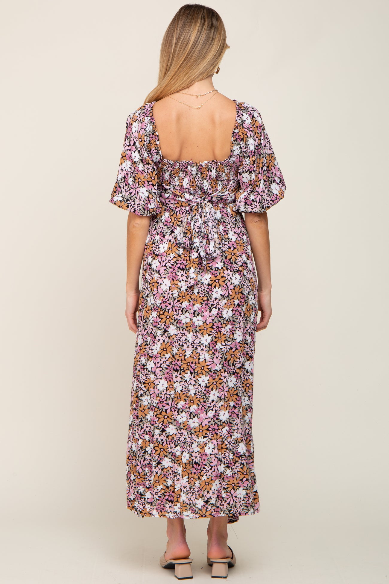 Back view of a woman wearing a pink and orange floral maxi dress with puff sleeves and a smocked tie back.