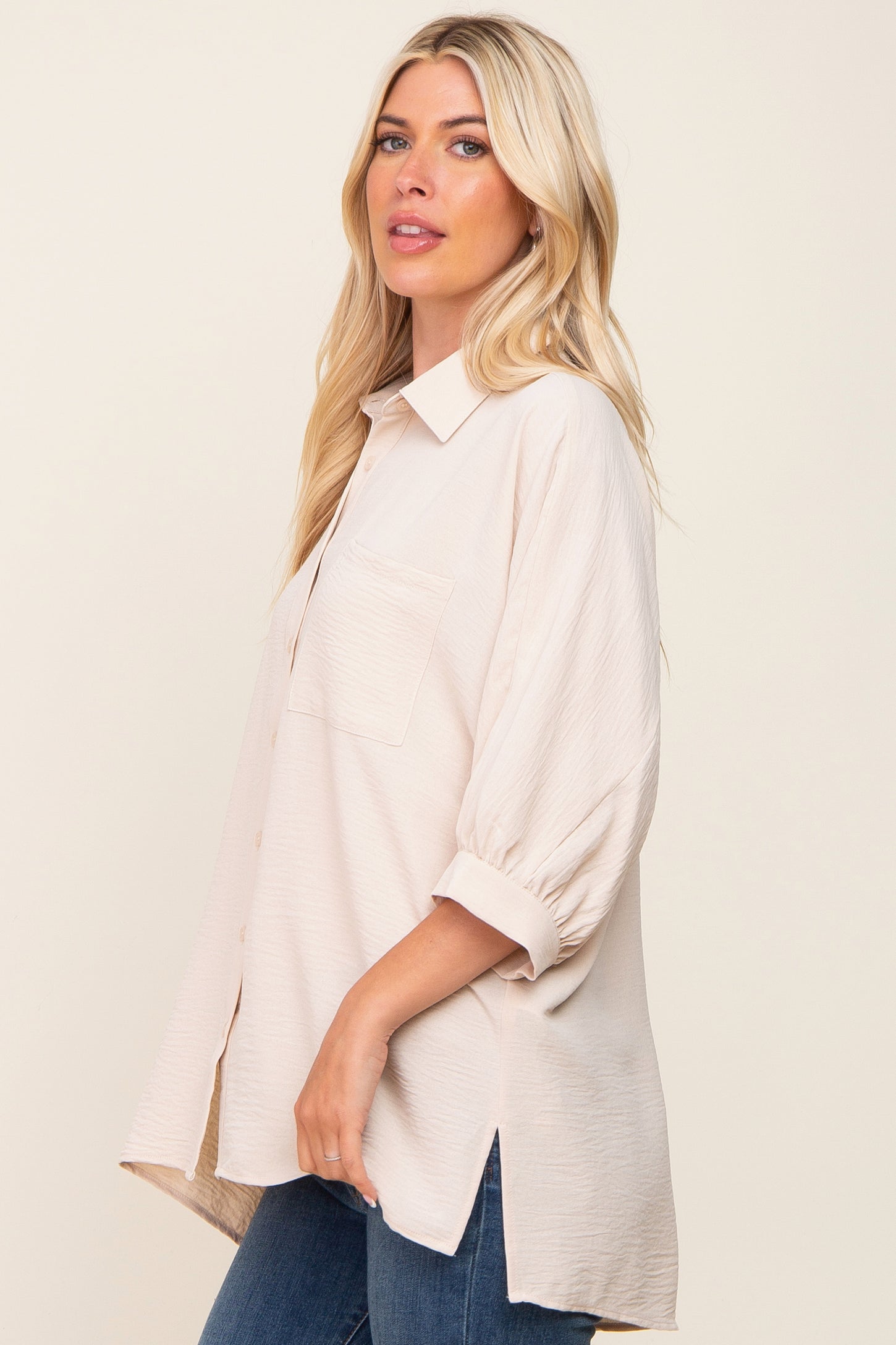 blonde woman wearing a cream oversized button-down shirt with three-quarter sleeves and blue jeans