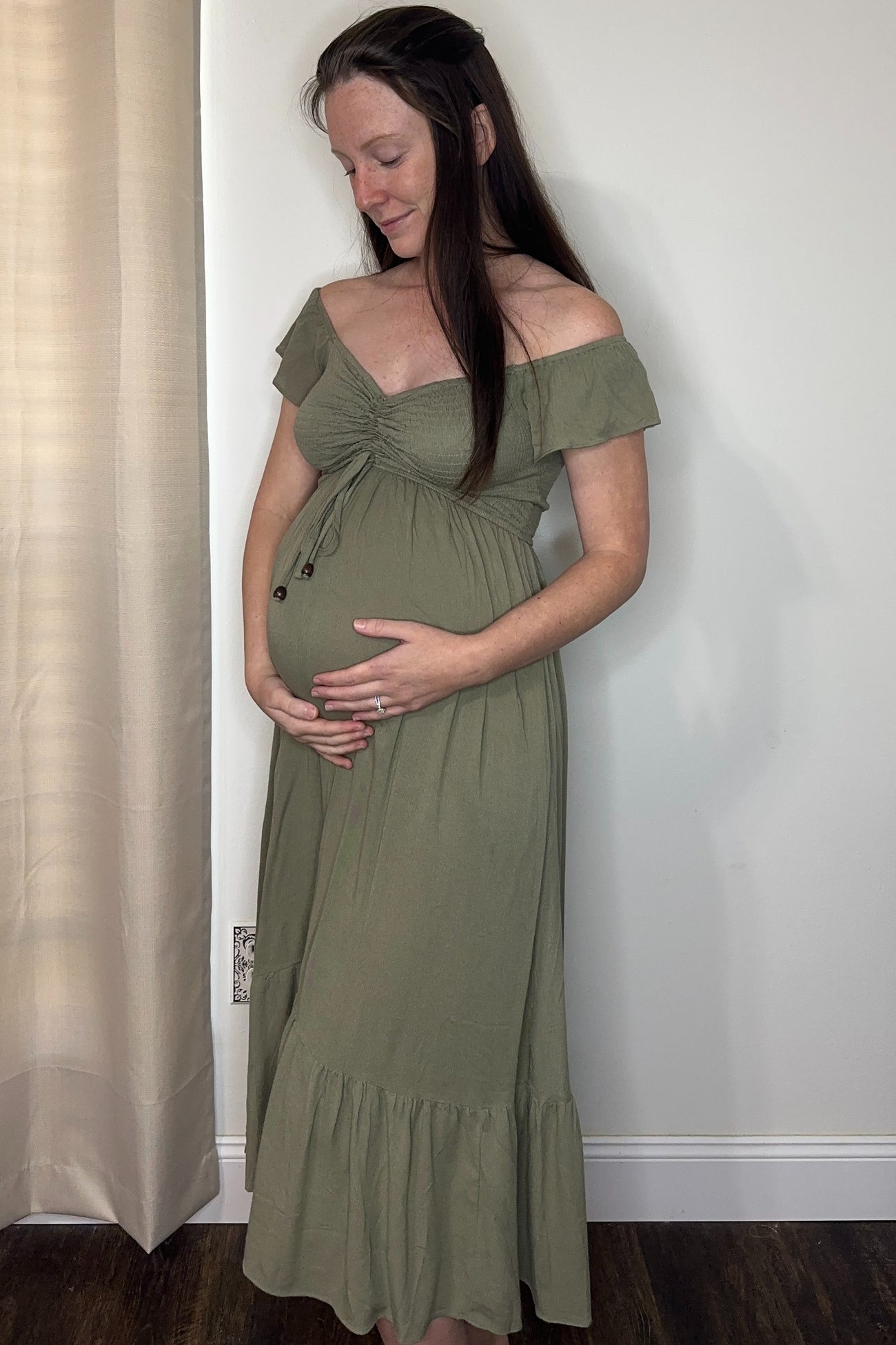 woman wearing an olive green off-the-shoulder maternity dress and holding her baby bump