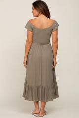 woman wearing a sage green off-the-shoulder maternity dress with a smocked bodice and ruffled hem, showing her back
