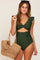 woman wearing a green one-piece swimsuit with ruffle sleeves and cut-out details, holding a woven tote bag