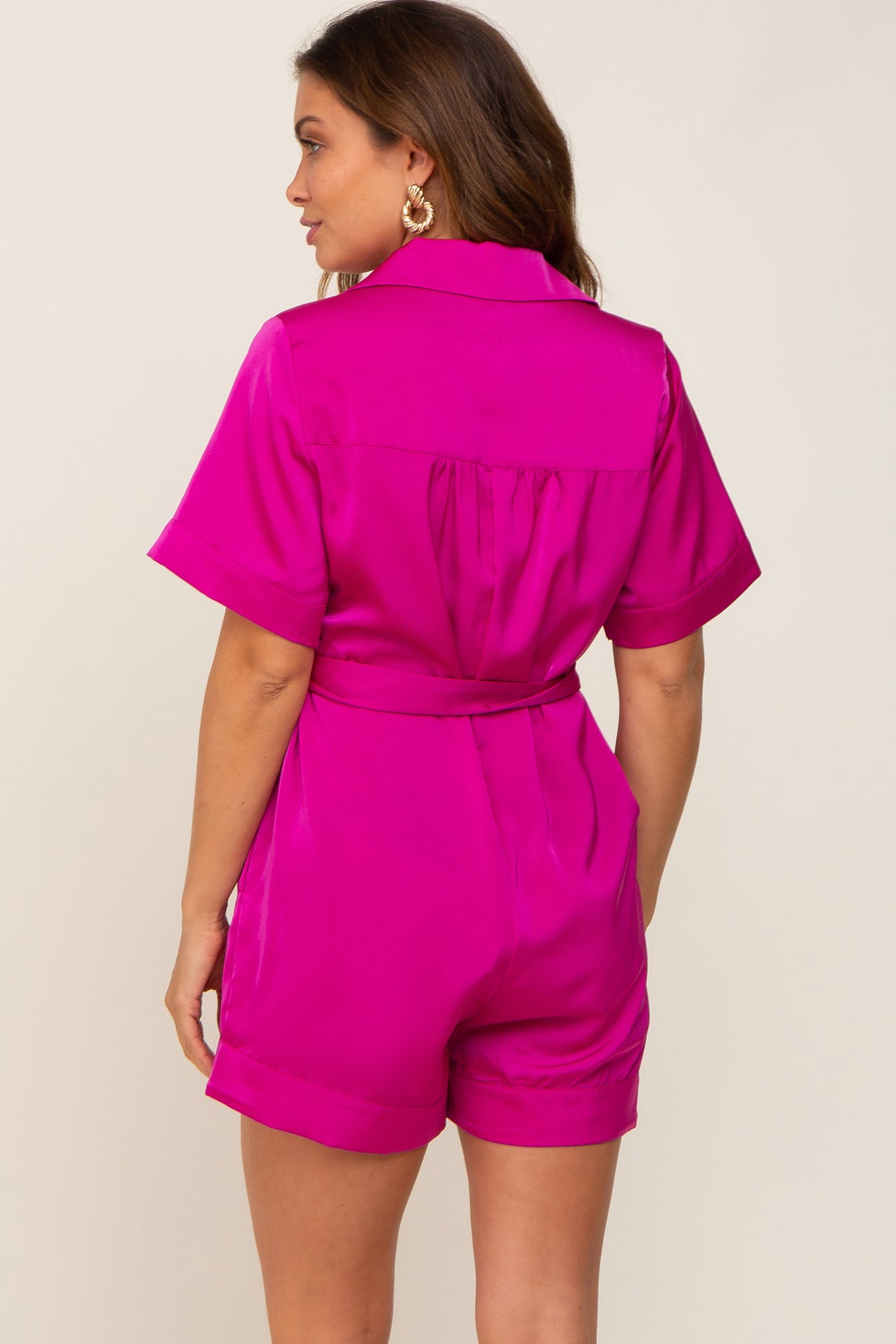 Back view of a woman wearing a vibrant magenta satin short-sleeve romper with a belted waist