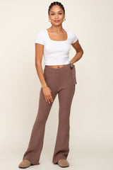 woman wearing a white square neck crop top and brown ribbed flared pants, posing with one hand on her hip