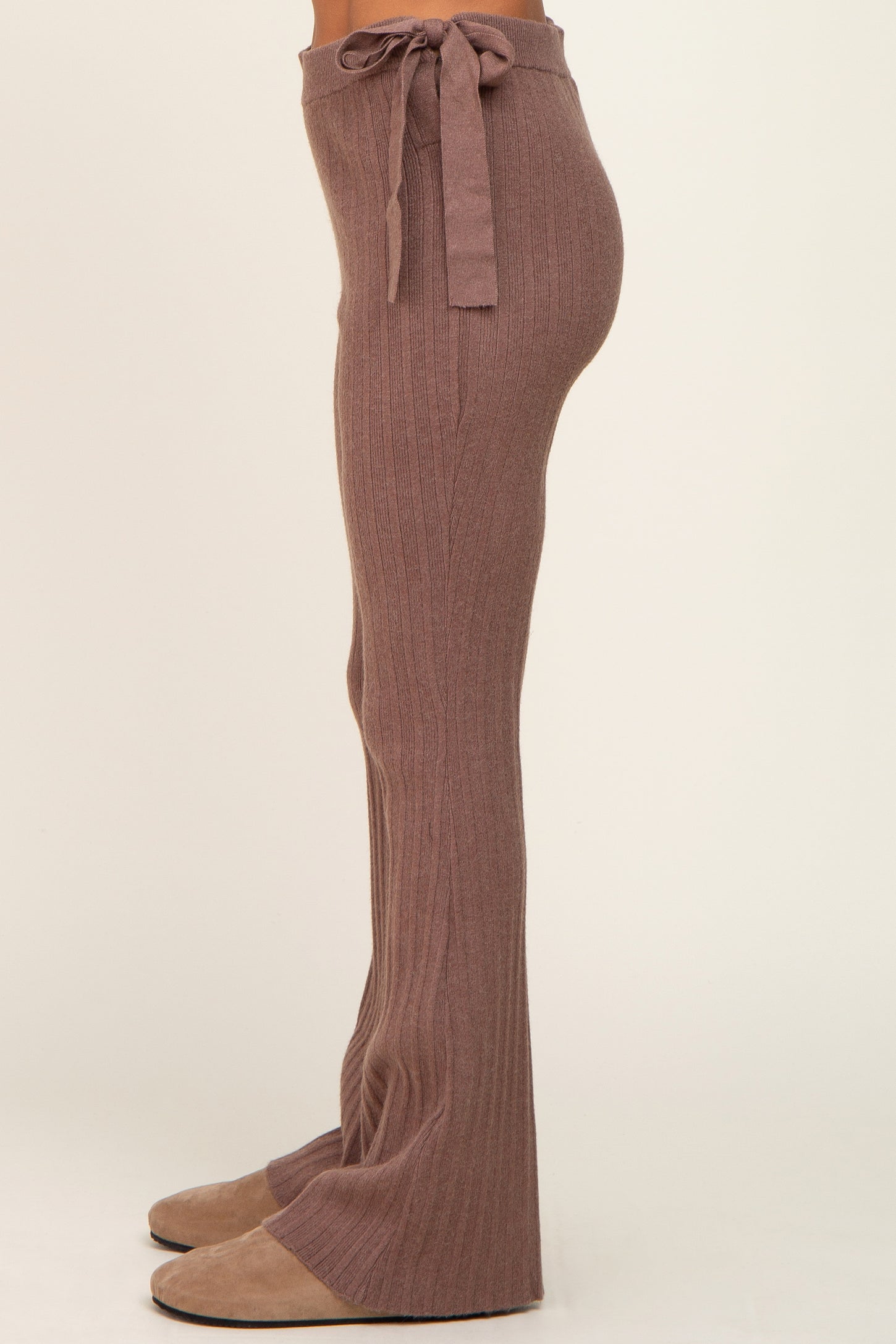 Side view of person wearing mauve ribbed knit flare pants with a tie waist and tan suede slippers