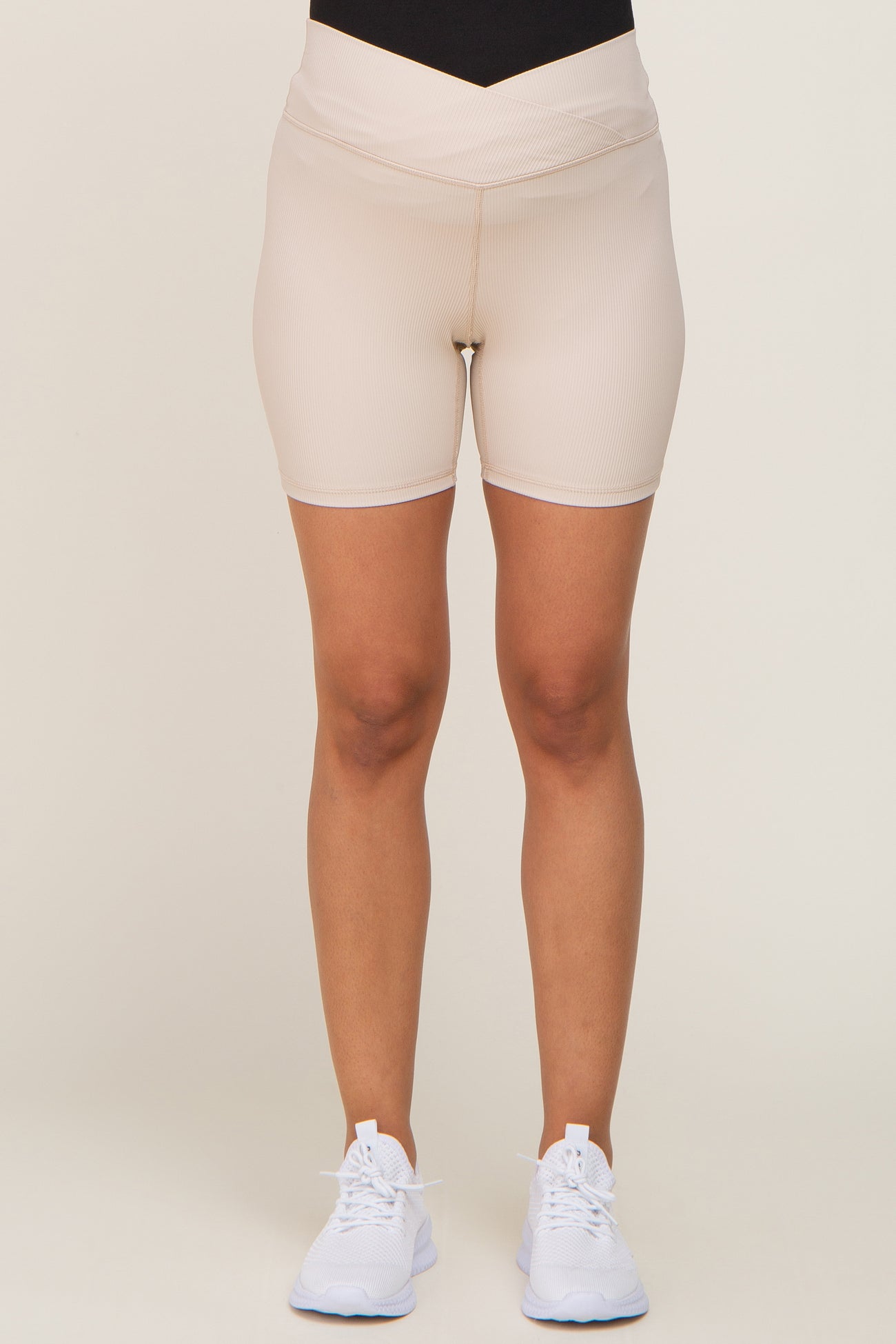 woman wearing beige maternity cycling shorts with a supportive waistband and paired with white athletic shoes