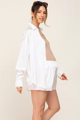 Pregnant woman wearing white satin button-down shirt and matching shorts with a tan maternity tank top