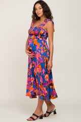 pregnant woman in a colorful blue and pink floral smocked maternity midi dress with tie straps