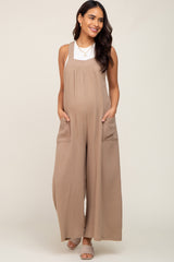 pregnant woman wearing a tan gauze maternity jumpsuit with wide legs and side pockets over a white top