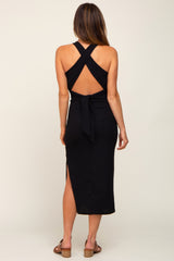 Back view of a woman wearing a black ribbed midi dress with a crisscross open back and tie waist detail