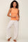 woman wearing a form-fitting orange ribbed tank top and white linen wide-leg pants, holding sunglasses