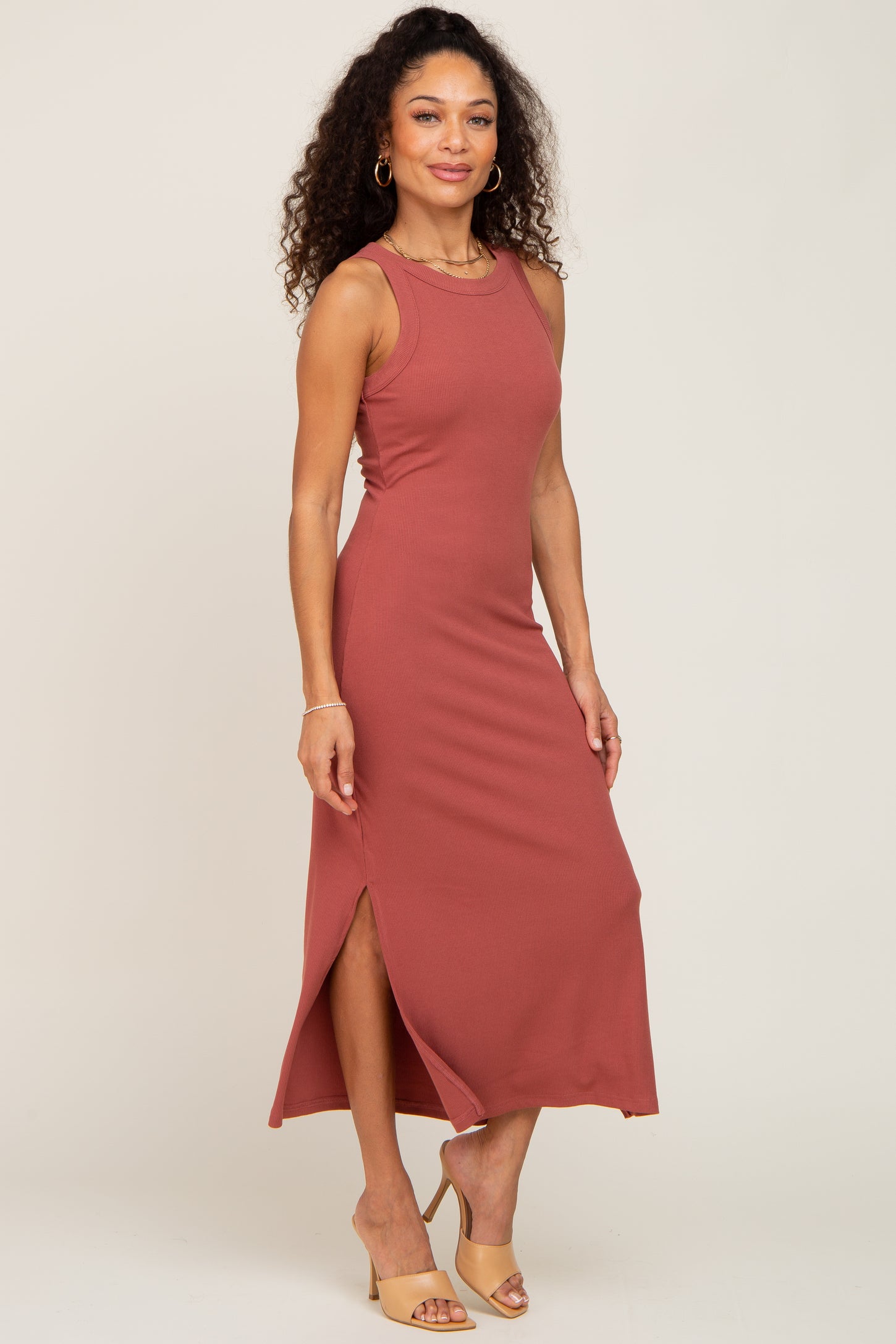 woman wearing a rust-colored sleeveless maxi dress with a side slit and a fitted silhouette