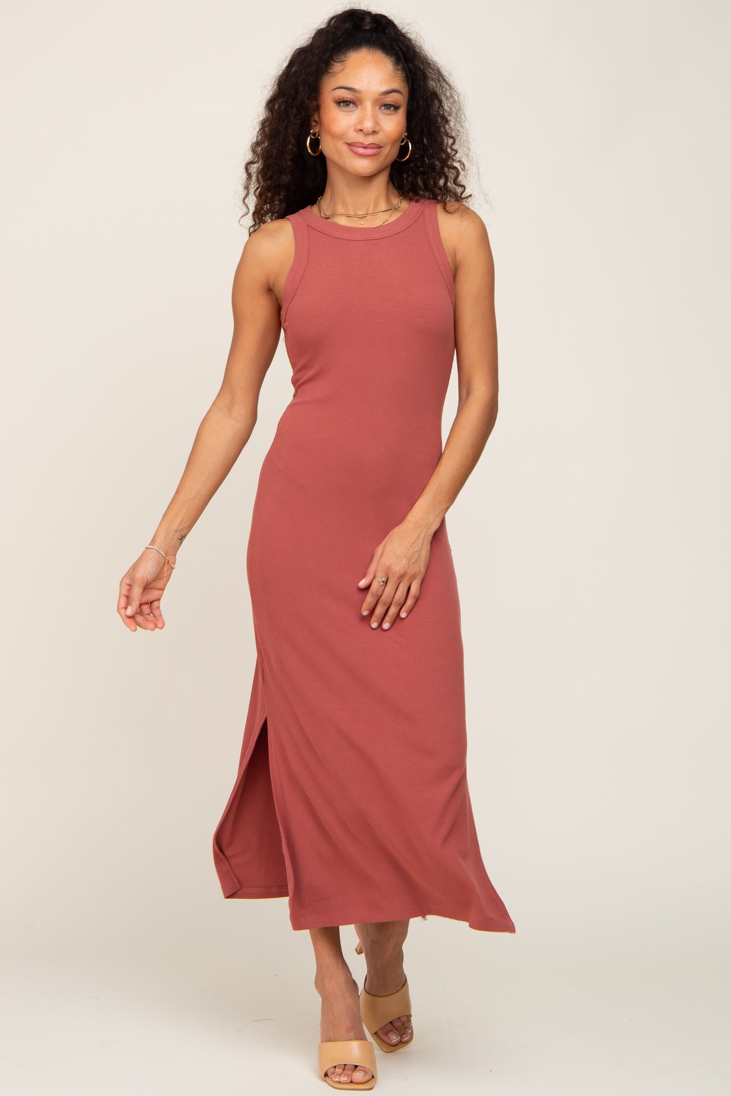 woman wearing a rust-colored sleeveless maxi dress with a side slit and casual sandals