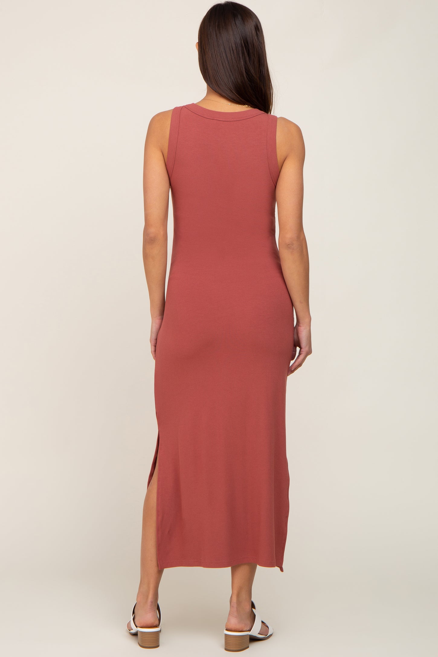 woman wearing a rust colored sleeveless ribbed maternity dress with a side slit, showing a smooth back view
