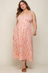 Pregnant woman wearing a pink floral smocked maternity midi dress with spaghetti straps