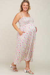 Smiling pregnant woman wearing a floral smocked maternity midi dress with pockets and white heels