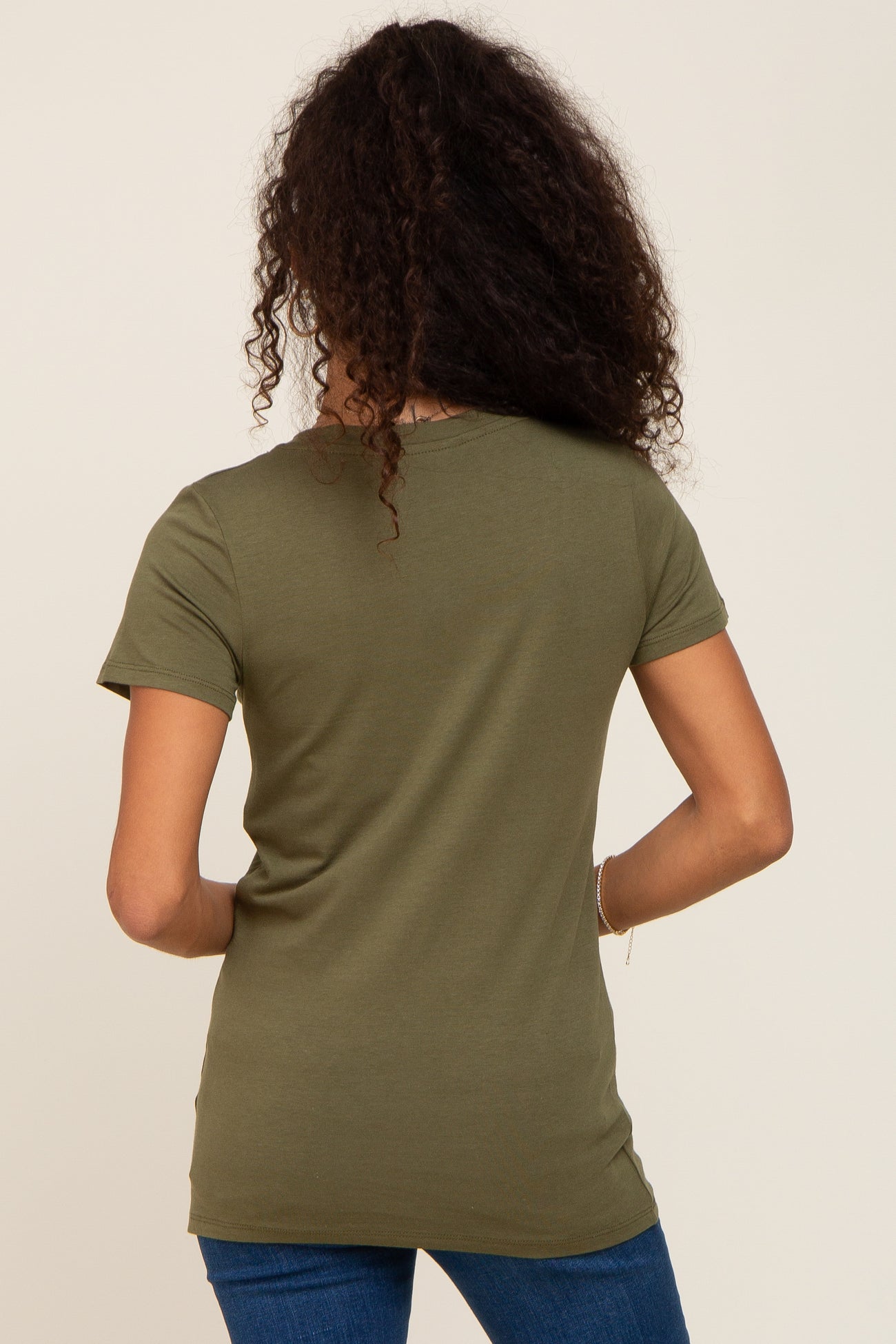 Back view of a woman with long curly hair wearing an olive green short sleeve t-shirt and blue jeans