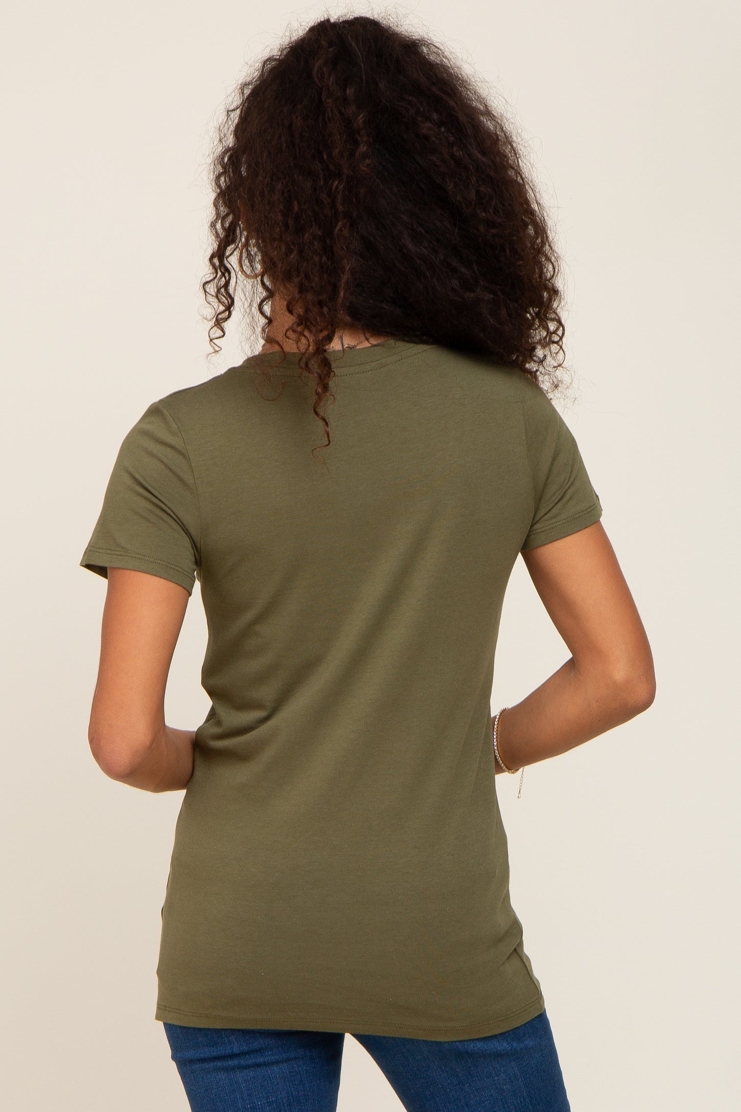 Back view of a woman with long curly hair wearing an olive green short sleeve t-shirt and blue jeans
