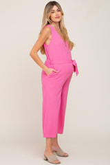 woman wearing a bright pink maternity jumpsuit with a tied waist and side pockets, showcasing her baby bump