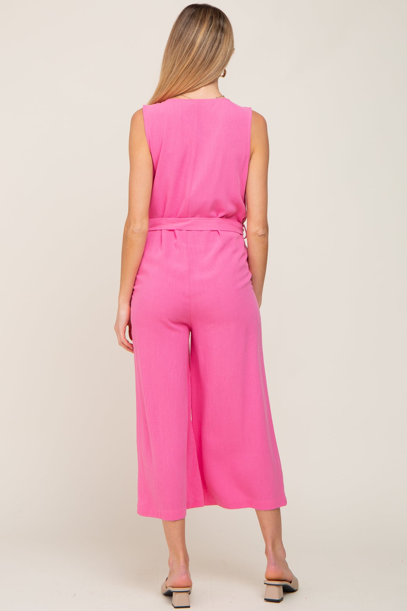 woman wearing a bright pink sleeveless maternity jumpsuit with wide legs and a belted waist, featuring a visible baby bump