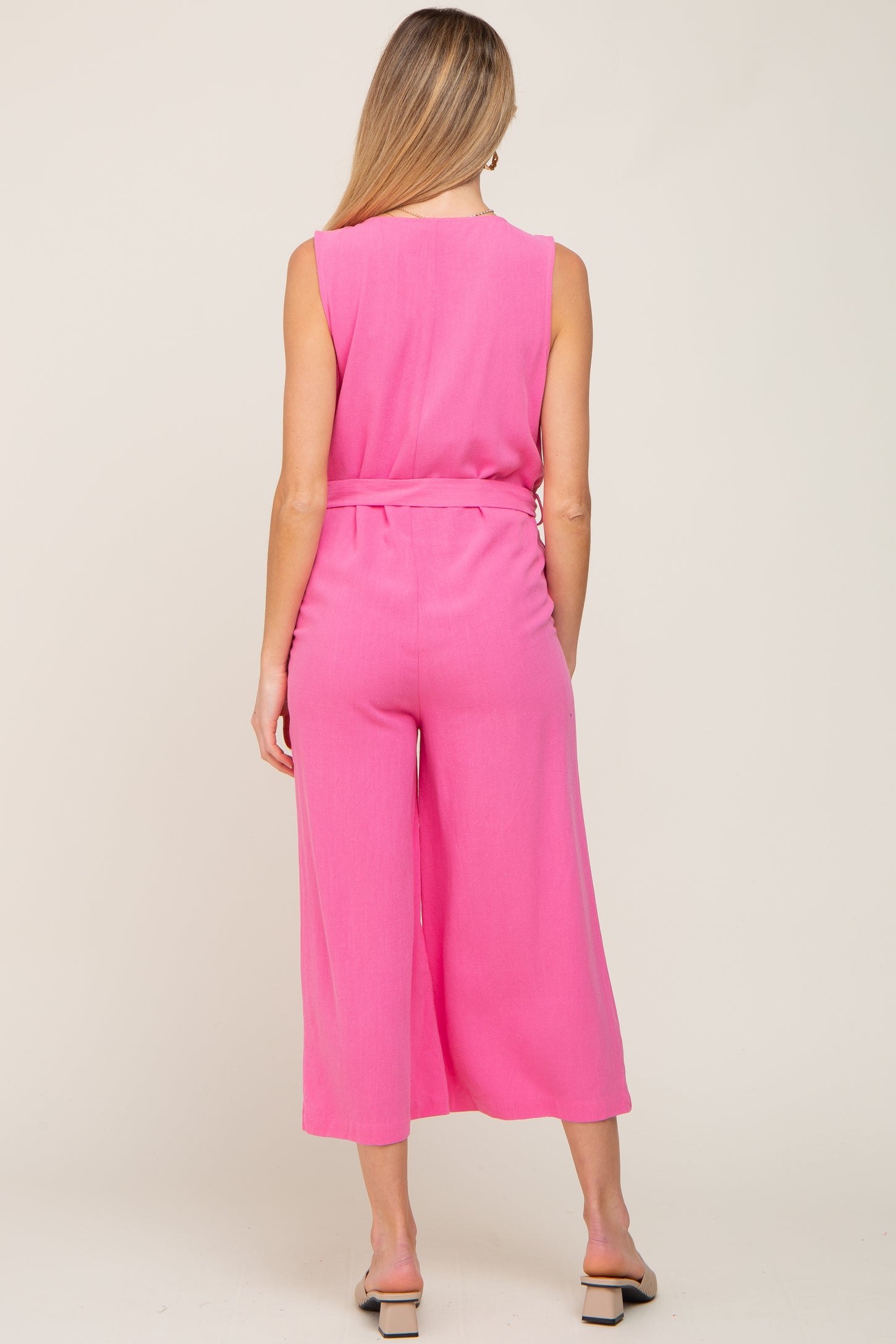 woman wearing a bright pink sleeveless maternity jumpsuit with wide legs and a belted waist, featuring a visible baby bump