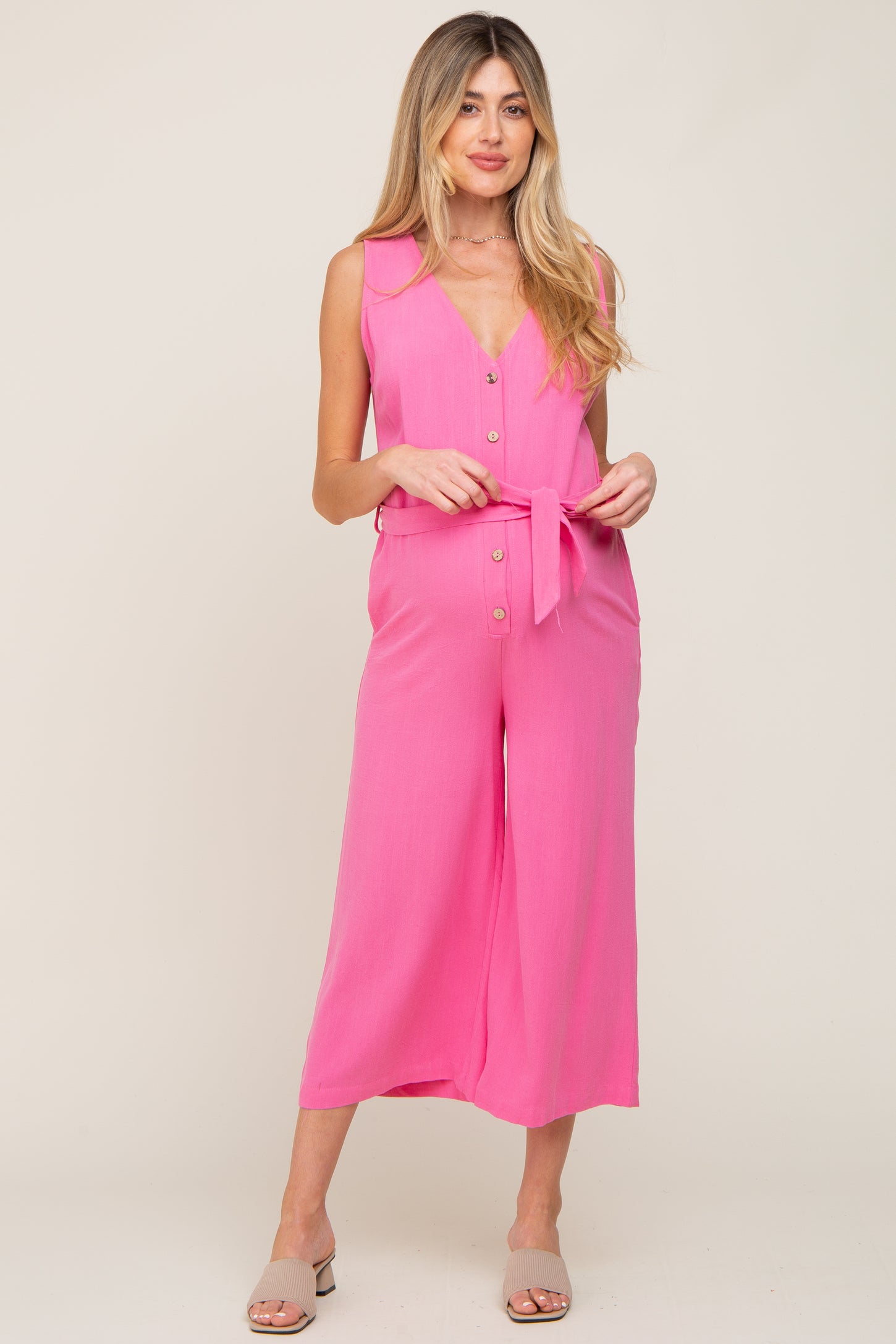 woman wearing a pink sleeveless maternity jumpsuit with buttons and a tie waist