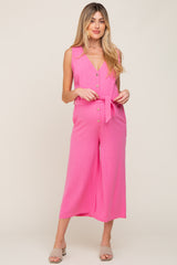 woman wearing a pink sleeveless maternity jumpsuit with buttons and a tie waist