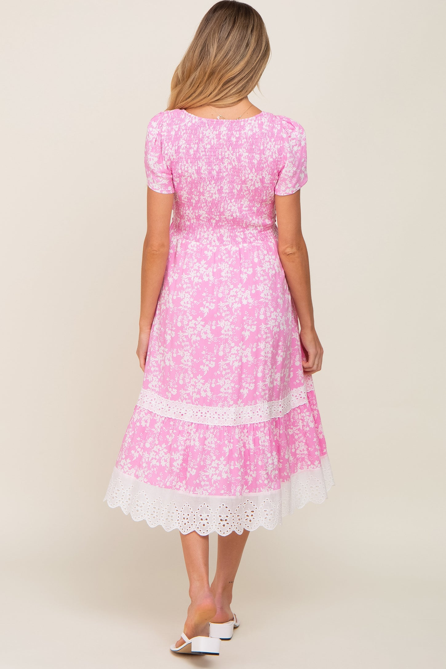 Back view of a woman wearing a pink floral midi dress with smocked bodice and white eyelet lace trim.