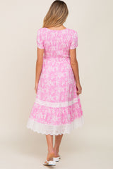 Back view of a woman wearing a pink floral midi dress with smocked bodice and white eyelet lace trim.