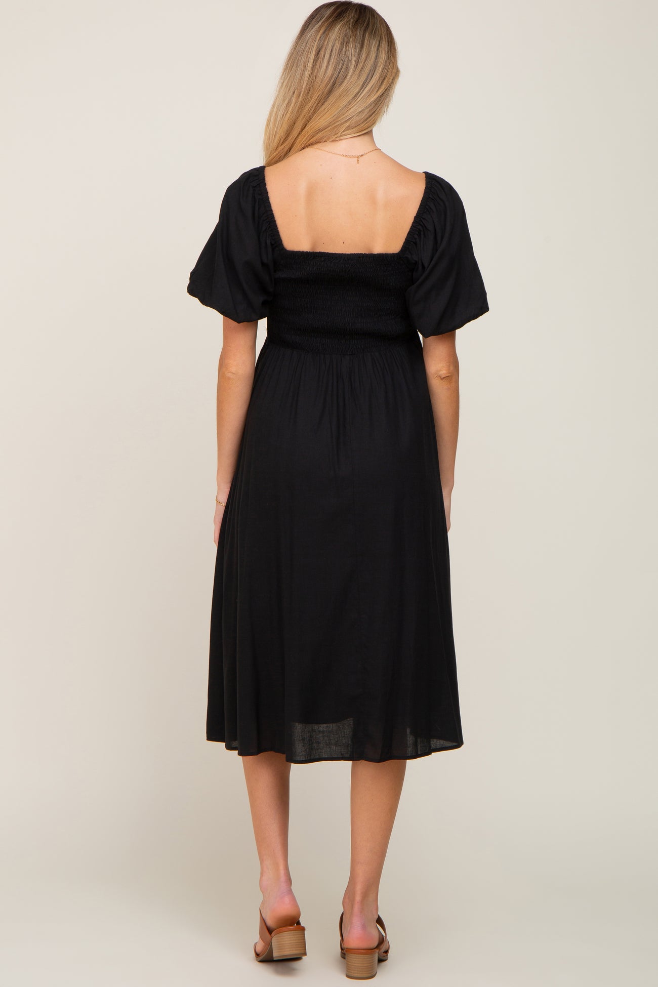 back view of woman wearing black smocked maternity midi dress with puff sleeves and square neckline