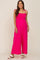 smiling pregnant woman wearing a bright pink maternity jumpsuit with tie straps and white sandals