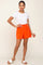 woman wearing white t-shirt and bright orange high-waisted shorts with white slide sandals
