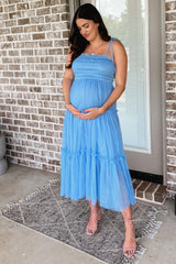 pregnant woman in a blue smocked tulle maternity dress holding her baby bump in front of a brick wall