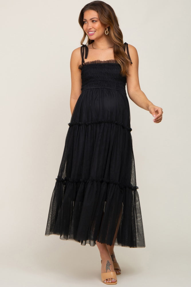 woman wearing a black tiered tulle maternity midi dress with tie straps and smocked bodice